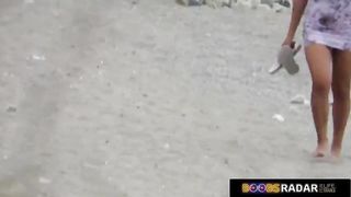 Nude lady is lying on the beach, while a horny voyeur is watching her shaved pussy